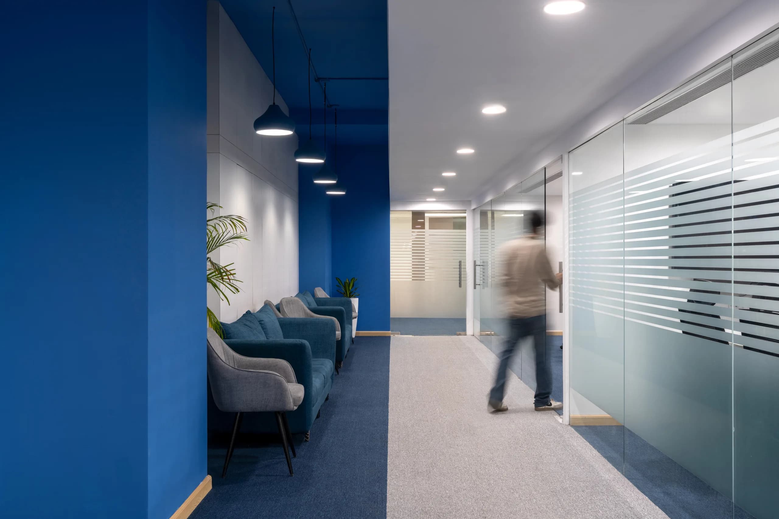 Blue-walled corridor with lounge seating and glass partitions, Blue Grid Workspace